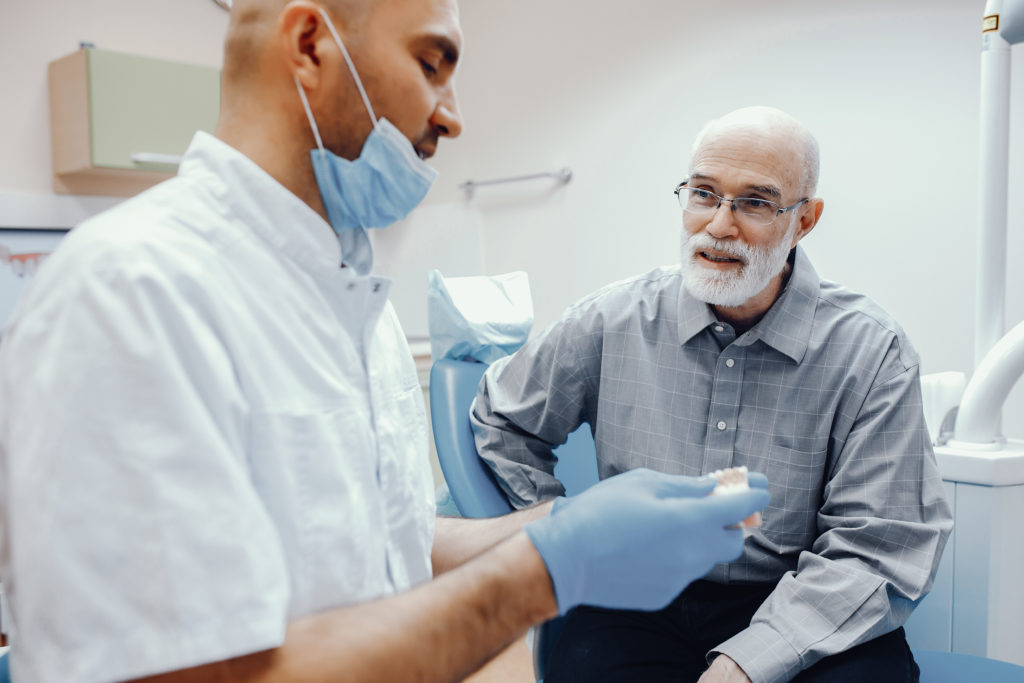 Elderly man sitting in dental office talking with one of Rubicare's providers.